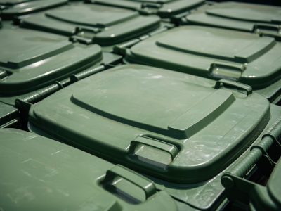 Daudzi zaļi plastmasas atkritumu konteineru vāki izvietoti rindās, redzami tuvplānā.